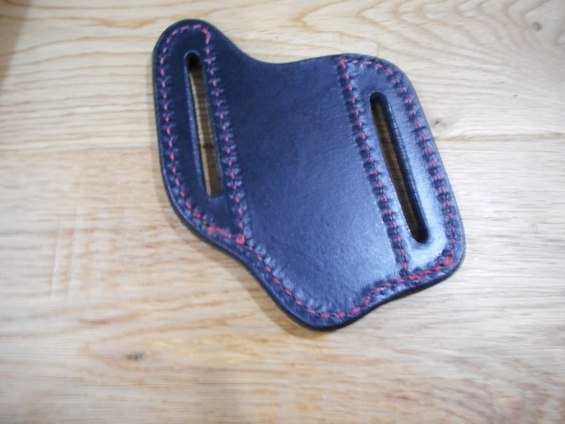 May include: A black leather knife sheath with red stitching. The sheath has two belt loops.