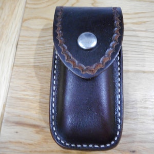 May include: A brown leather pocket knife case with white stitching and a silver snap closure.