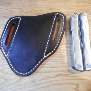 May include: A brown leather sheath with white stitching for a multi-tool. The sheath has two belt loops. The multi-tool is silver with a black handle and the text "Leatherman" printed on the side.