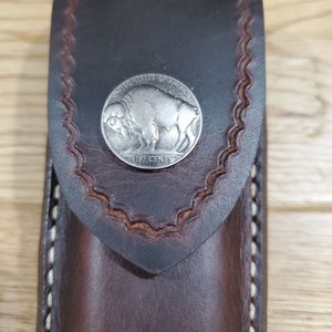 Peut inclure: Un &eacute;tui en cuir marron avec des d&eacute;tails de couture blancs. Une pi&egrave;ce de monnaie en nickel de buffle argent&eacute;e est fix&eacute;e &agrave; l'avant de l'&eacute;tui.