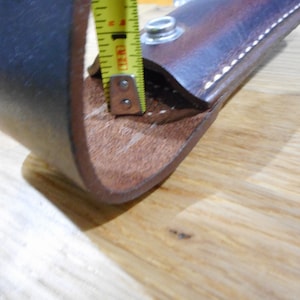 Peut inclure: Une boucle de ceinture en cuir marron avec un bord cousu et un bouton-pression en m&eacute;tal. La boucle est mesur&eacute;e avec un ruban &agrave; mesurer jaune.