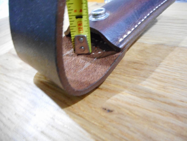 Peut inclure: Une boucle de ceinture en cuir marron avec un bord cousu et un bouton-pression en m&eacute;tal. La boucle est mesur&eacute;e avec un ruban &agrave; mesurer jaune.