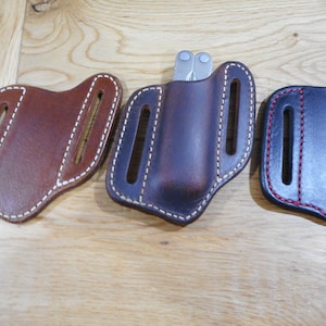 May include: Three leather sheaths for multi-tools. The sheaths are brown, dark brown, and black. Each sheath has a belt loop and a stitched design.