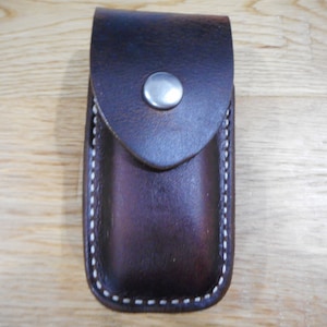 May include: A brown leather case with a white stitch detail and a silver snap closure.