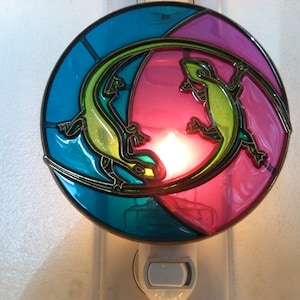 May include: A nightlight with a stained glass design featuring two green lizards on a blue and pink background.