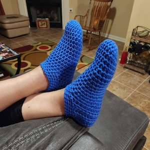 May include: A pair of blue crocheted slipper socks. The socks are made with a simple stitch pattern and have a comfortable fit.