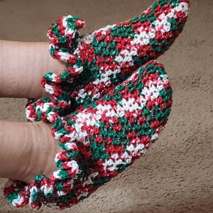 May include: A pair of red, green, and white crocheted slipper socks with a ruffled trim.