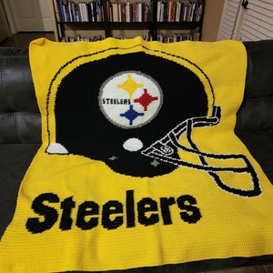 May include: A yellow and black crocheted blanket featuring a Pittsburgh Steelers helmet and the team name "Steelers".