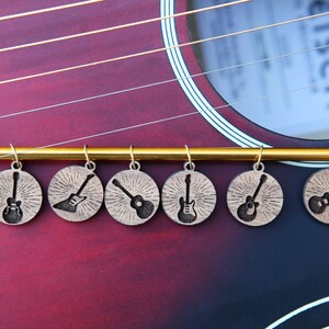 May include: A set of six wooden guitar-shaped charms with a gold metal bar. Each charm features a different silhouette of a guitar with a sunburst design.