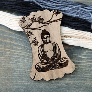 May include: Wooden thread holder with a laser-engraved design of a meditating Buddha sitting under a tree with flowers.
