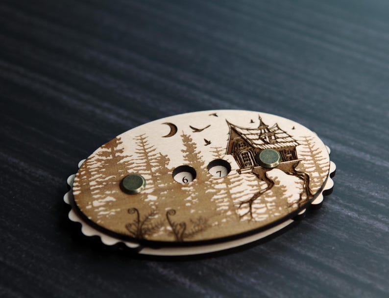 May include: Oval wooden game piece with a forest and house design. The piece has a scalloped edge, two embedded magnets, and the numbers 6 and 7. The artwork includes a moon, birds, and trees.