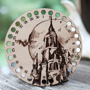 May include: A wooden circular stitch marker with 30 holes, numbered 1-30. The marker features a black and white illustration of a castle with a full moon and a bat flying overhead.