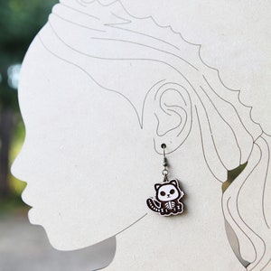 May include: A pair of silver dangle earrings with a black and white cartoon skeleton cat charm.