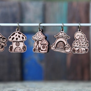 May include: Six wooden mushroom house charms with intricate details, hanging from a white string. Each charm features a different design, including a mushroom with a door and windows, a mushroom with a spiral top, and a mushroom with a pointed cap.