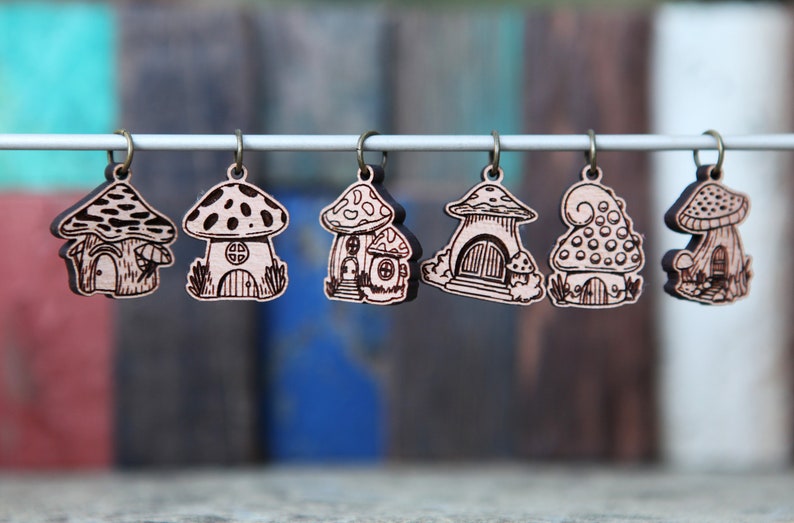 May include: Six wooden mushroom house charms with intricate details, hanging from a white string. Each charm features a different design, including a mushroom with a door and windows, a mushroom with a spiral top, and a mushroom with a pointed cap.