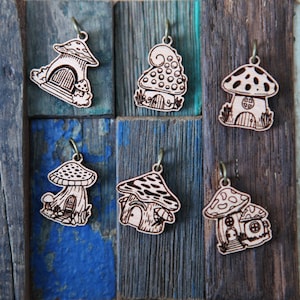 May include: Six wooden mushroom house charms with intricate details. Each charm features a different design, including a mushroom with a door, a mushroom with a window, and a mushroom with a chimney. The charms are all made of natural wood and have a rustic, whimsical look.