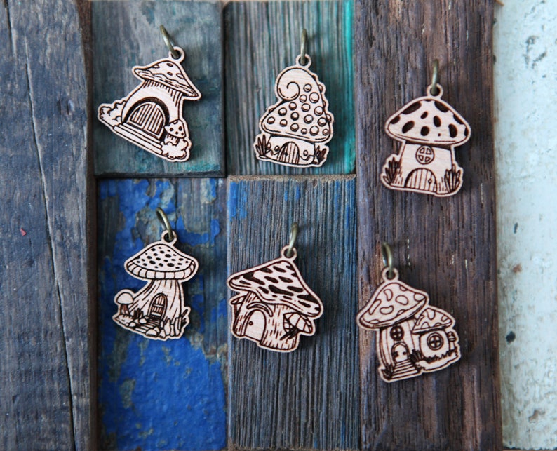 May include: Six wooden mushroom house charms with intricate details. Each charm features a different design, including a mushroom with a door, a mushroom with a window, and a mushroom with a chimney. The charms are all made of natural wood and have a rustic, whimsical look.