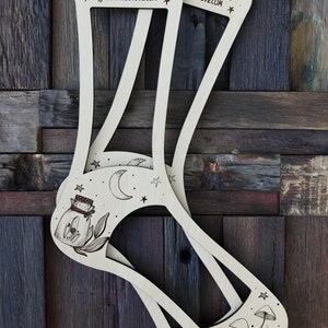 May include: Two wooden sock blockers with a moon, stars, and a jar with a flower design on one side and mushrooms on the other side. The text "Sunrise Grove Knittery sunrisegrove.com" is engraved on the blockers.