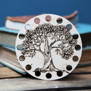 May include: A wooden circular knitting needle holder with a tree design burned into the surface. The holder has 12 holes around the edge for needles.