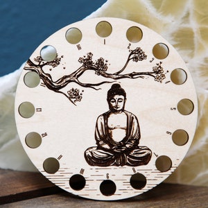 May include: Wooden thread holder with 16 holes, featuring a laser-etched design of a meditating Buddha under a blossoming tree branch.