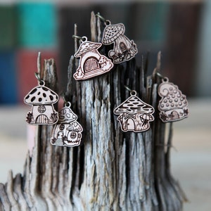 May include: Six wooden mushroom charms with intricate details, each featuring a small house-like structure with a door and windows. The charms are painted in a light brown color and have a rustic, whimsical aesthetic.