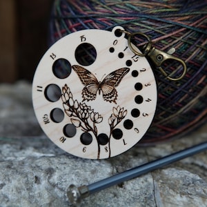 May include: Wooden circular needle minder with 15 holes and a butterfly design. The minder has a metal clip for attaching to a project.