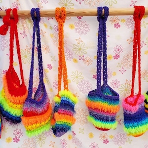 May include: Five colorful crocheted bags hanging from a wooden rod. The bags are made with rainbow colored yarn and have a fluffy texture.