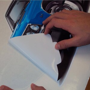 May include: A blue and black car decal with a white backing being peeled off. The decal is a detailed illustration of a classic car.