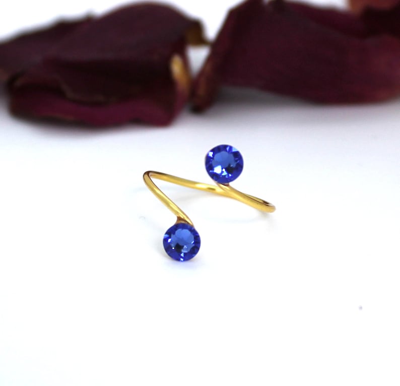 May include: Gold ring with two blue gemstones. The ring is twisted and has a simple design.