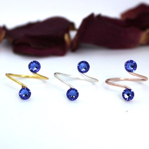 May include: Three gold, silver, and rose gold rings with blue gemstones. Each ring has a twisted band and two blue gemstones.