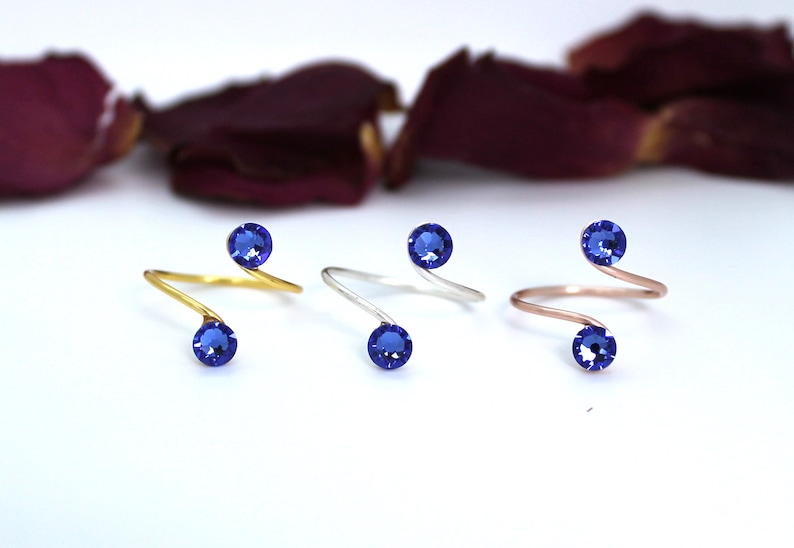 May include: Three gold, silver, and rose gold rings with blue gemstones. Each ring has a twisted band and two blue gemstones.