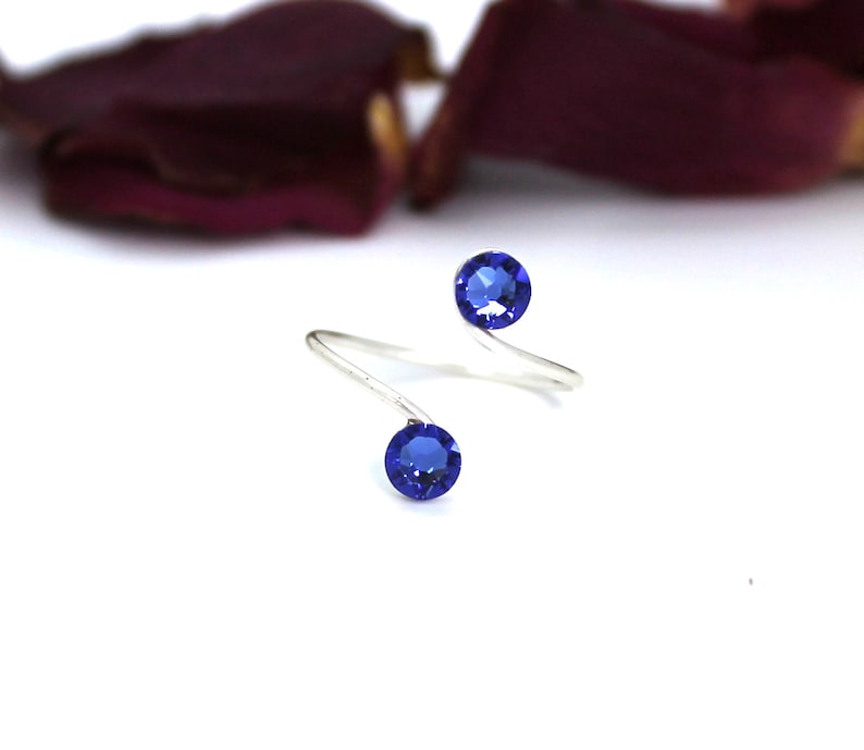 May include: A silver ring with two blue gemstones. The ring is twisted and has a simple design.
