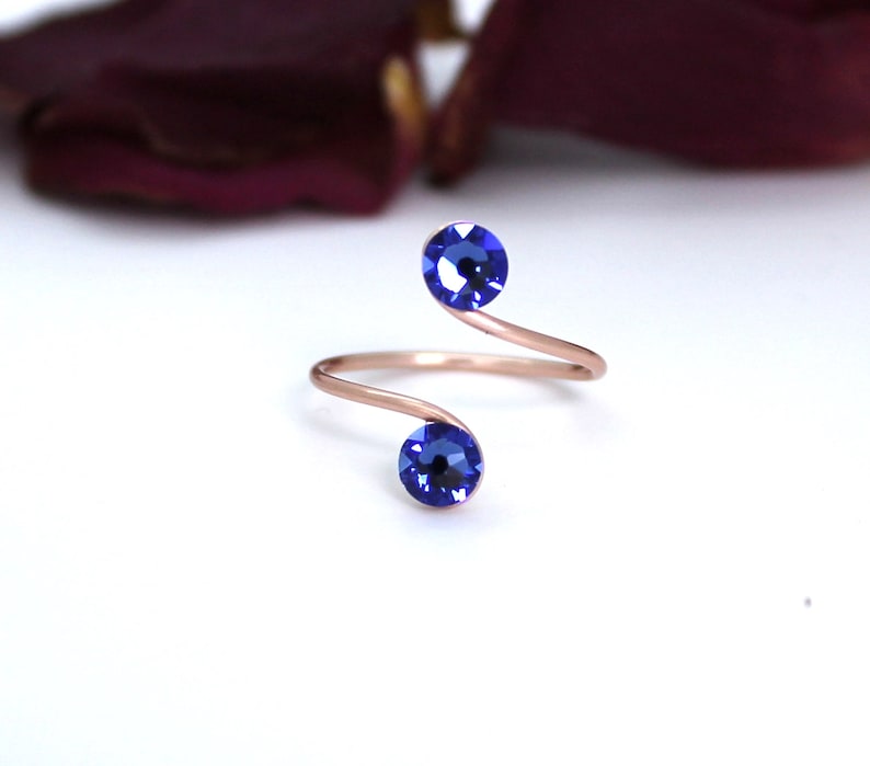 May include: A rose gold ring with a twisted band and two blue crystal accents.