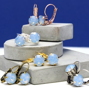 May include: Assortment of earrings with light blue opal stones. The earrings are displayed on a stack of gray concrete blocks. The earrings have different styles of ear wires, including leverback, hook, and post.