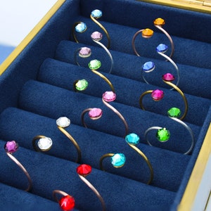 Peut inclure: Un coffret à bijoux doublé de velours bleu avec une bordure dorée, contenant une collection de bracelets en spirale dorés avec des accents de cristal colorés.