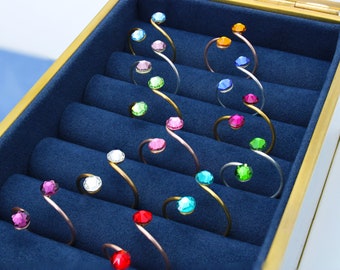 May include: A blue velvet-lined jewelry box with a gold trim, containing a collection of gold-toned, spiral-shaped bracelets with colorful crystal accents.