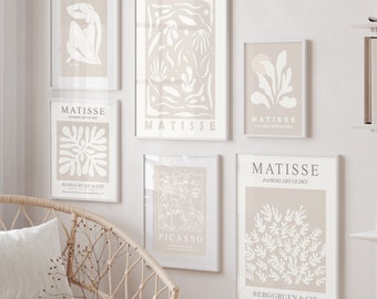 Puede incluir: Un conjunto de seis impresiones de arte enmarcadas en una gama de colores beige neutro. Las impresiones presentan diseños abstractos en blanco sobre un fondo beige. Las impresiones están dispuestas en una pared blanca con una unidad de estantería blanca y una silla de mimbre con un cojín blanco.
