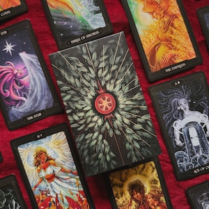 May include: A deck of tarot cards featuring a central box with a pomegranate illustration surrounded by green leaves and radiating lines. Surrounding cards display colourful, detailed illustrations including The Empress, The Star, and Six of Wands.