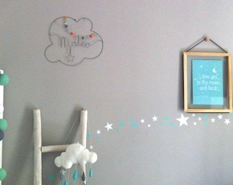 May include: A nursery wall scene with a grey wall, featuring a framed print with the text "I love you to the moon and back." A cloud-shaped wire art piece with the name "Mateo" and a star mobile hangs nearby. Decorative star stickers are also present.