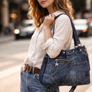 Puede incluir: Un bolso de mano de mezclilla azul con múltiples bolsillos y un dije en forma de estrella. El bolso tiene una correa para el hombro y un cierre de cremallera. El bolso es de mezclilla azul y tiene un cinturón de cuero marrón.