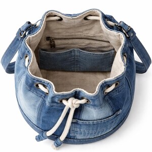 May include: A denim bucket bag with a drawstring closure and shoulder straps. The bag features a patchwork design of various shades of blue denim. The interior is lined with a light-coloured fabric and includes a zipped pocket and a slip pocket.