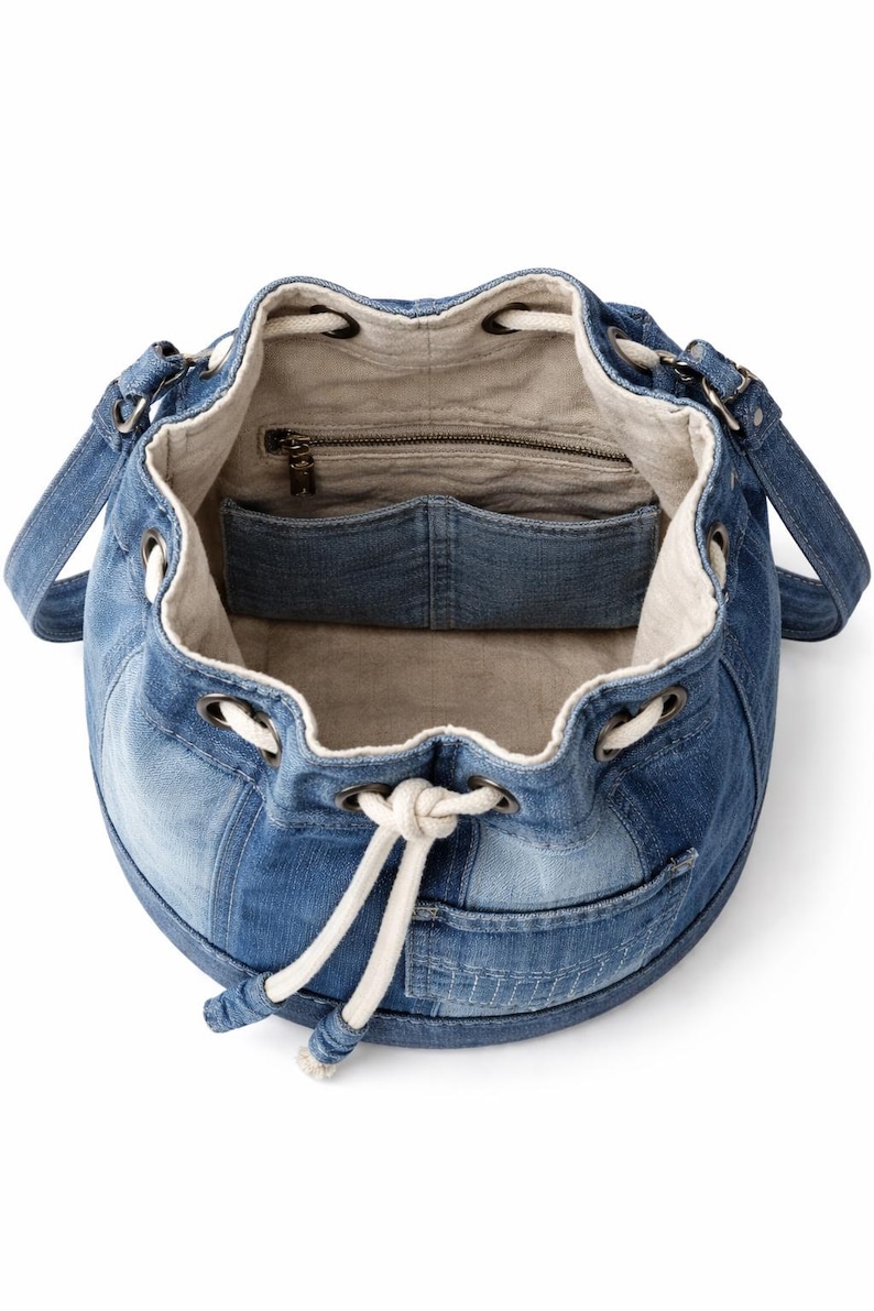 May include: A denim bucket bag with a drawstring closure and shoulder straps. The bag features a patchwork design of various shades of blue denim. The interior is lined with a light-coloured fabric and includes a zipped pocket and a slip pocket.