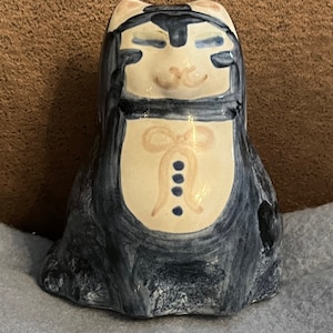 Puede incluir: Figura de gato de cerámica con cara color crema y cuerpo azul oscuro. El gato tiene los ojos cerrados, nariz rosa y diseño de pajarita en el pecho. La figura está pintada a mano con acabado brillante.