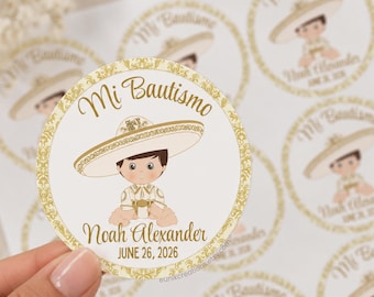 May include: A round sticker featuring a cartoon child wearing a white sombrero and traditional outfit. The text reads Mi Bautismo, Noah Alexander, and JUNE 26, 2026. The sticker has a gold decorative border and is part of a sheet of identical labels.