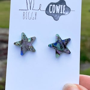 May include: A pair of iridescent blue and green star-shaped earrings on a white card with the text "Me Biggy Cowie" printed on it.