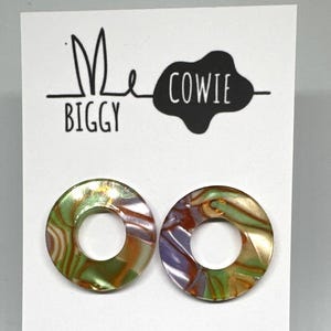 May include: A pair of round, iridescent earrings with a green, purple and gold swirl pattern. The earrings are on a white card with the text "Me Biggy Cowie" on it.