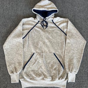 May include: A gray hooded sweatshirt with a navy blue interior and trim. The sweatshirt has a front pocket and drawstring. The cuffs and waistband are ribbed. A casual, comfortable garment for everyday wear.