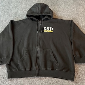 May include: Black zip-up hoodie with a hood and front pockets. The text "CSI: LAS VEGAS UNIT" is printed on the chest in yellow and white. The hoodie is made of a thick, durable material.