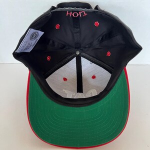 May include: Black and green baseball cap with a red brim. The cap has a white inner lining and the words "HOP" and "TAG" are embroidered on the front and back of the cap.