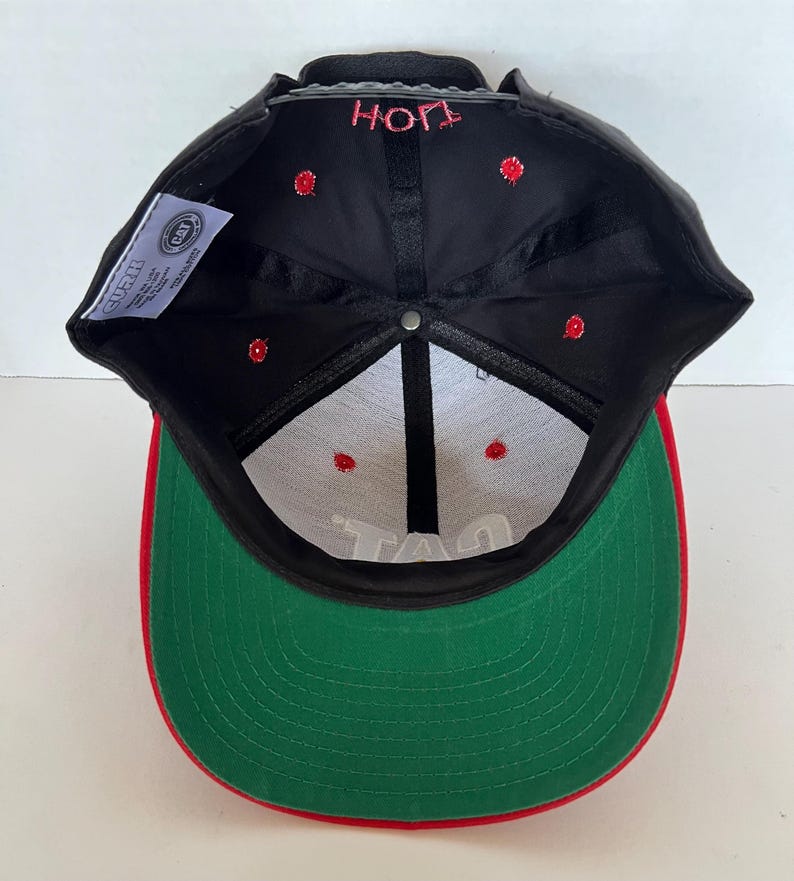 May include: Black and green baseball cap with a red brim. The cap has a white inner lining and the words "HOP" and "TAG" are embroidered on the front and back of the cap.